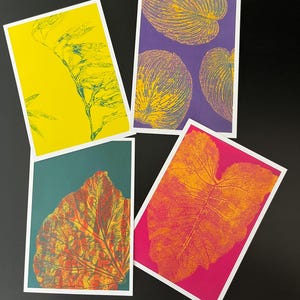May include: Four rectangular art prints featuring botanical leaf patterns. One print has a yellow background with green foliage, another a purple background with yellow leaves, one a teal background with a red-orange leaf, and one a pink background with orange leaves.