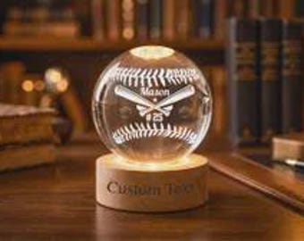 Peut inclure: Une sphère en verre transparent gravée d'un motif de baseball, de battes croisées, du nom Mason et du numéro 25. La sphère repose sur une base en bois circulaire portant le texte gravé Custom Text, éclairée par une source lumineuse interne.