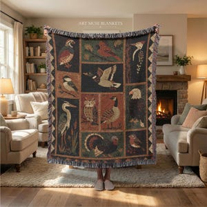 May include: A woven throw blanket featuring a grid of various bird illustrations including a mallard, owl, and eagle, with the text ART MUSE BLANKETS at the top. The blanket has a dark background with earthy tones and a fringed edge on all sides.