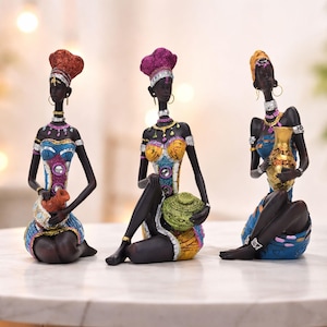 May include: Three decorative figurines of seated African women. Each figure has dark skin, ornate clothing, and a headdress. The figures hold decorative vessels in their laps. The color palette includes blue, gold, purple, and orange.