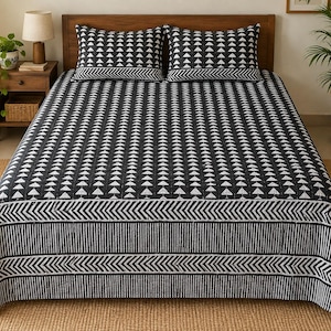 May include: A black and white bedspread featuring a repeating pattern of small triangles across the main surface, bordered by horizontal bands of chevron and vertical stripes. Two matching rectangular pillows are placed at the head of the bed.