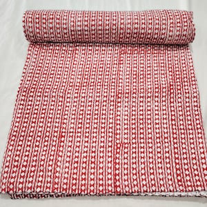 Pode incluir: Um edredom enrolado com um padrão vermelho e branco. O edredom apresenta um padrão repetitivo de linhas verticais com detalhes em forma de diamante. O tecido é de cor vermelha lisa com detalhes brancos. O edredom é dobrado e enrolado no topo.