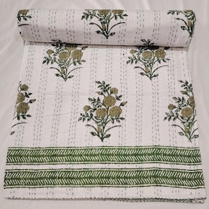 Könnte beinhalten: Weißes Steppbett mit olivgrünem Blumenmuster. Das Design zeigt sich wiederholende Blumenmotive und einen grünen geometrischen Rand. Das Steppbett ist aufgerollt und zeigt das Muster. Die Maße sind nicht sichtbar.