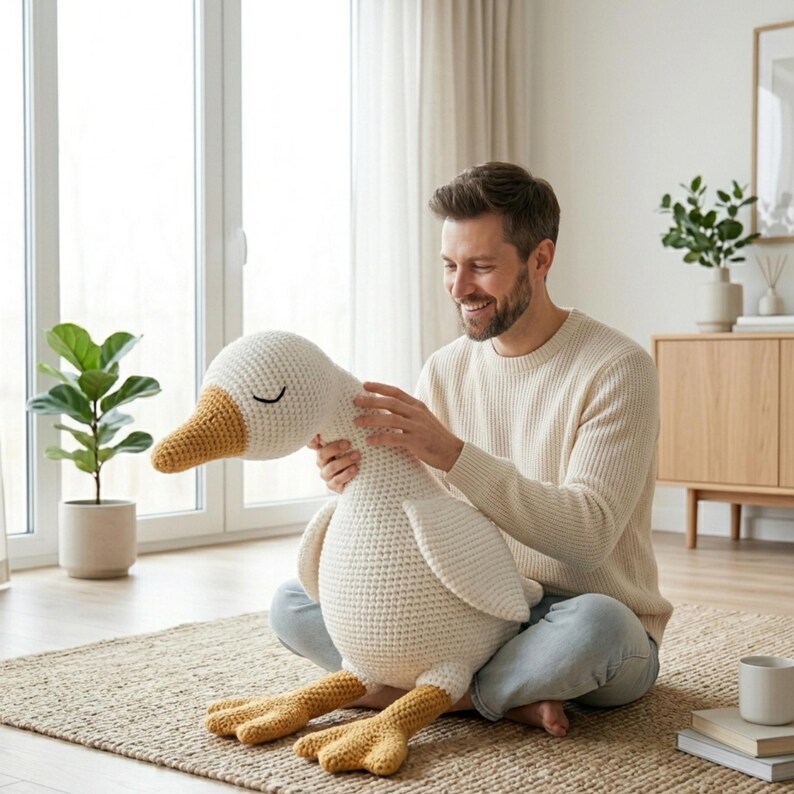 May include: A large, handmade crochet goose plush toy. The goose is primarily white with a yellow beak and feet. It has closed eyes, suggesting a sleeping or relaxed pose. The toy is soft and cuddly, perfect for a child's room or as a decorative item.