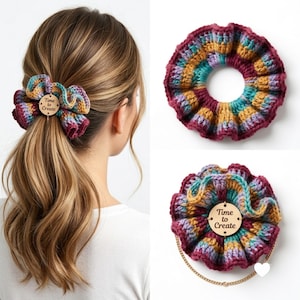 May include: A crocheted hair scrunchie featuring a variegated pattern of maroon, mustard yellow, teal, and lavender yarn. A circular wooden tag is attached to the center, engraved with the text Time to Create in a dark brown script font.
