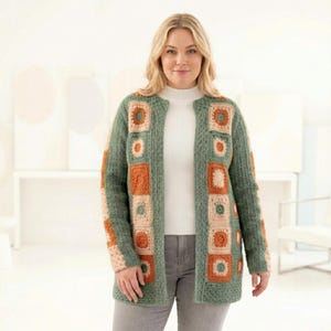 May include: A green crochet cardigan with square, floral, and geometric patterns in shades of orange and beige. The open-front cardigan is worn over a white top and gray pants. The cardigan has a textured knit design.