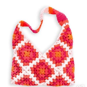 May include: A handmade crochet bag in a granny square pattern. The bag features a vibrant color palette of pink, orange, and white. The strap is a continuation of the crochet design. The bag is designed to be worn over the shoulder.