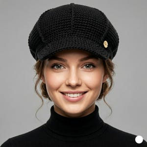 May include: A black, knitted newsboy cap with a rounded crown and a small, stiff brim. The cap has a gold-coloured button on the side. The person in the image is wearing a black turtleneck.