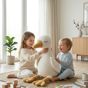 May include: A large, soft, white crochet goose with a yellow beak and feet. The plush toy is being held by two children. The goose has closed eyes and is sitting on a woven rug. The children are smiling and laughing.