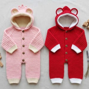 May include: Two handmade crochet baby rompers. One is pink with a crown-shaped hood and the other is red with a bear-shaped hood. Both have button closures and white and cream-colored accents. The rompers are designed for infants.