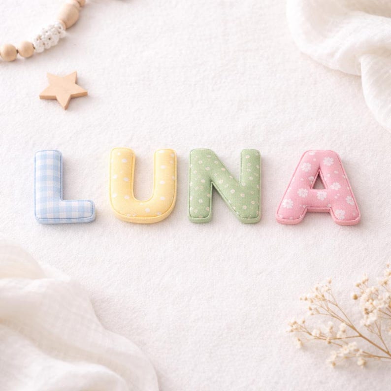 May include: The name "LUNA" is spelled out with colorful fabric letters. The letter "L" is light blue gingham, "U" is yellow with white polka dots, "N" is green with white polka dots, and "A" is pink with white flowers.