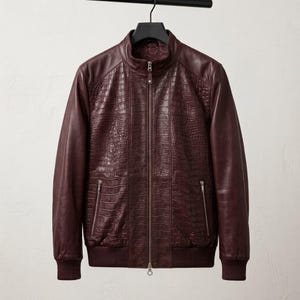 May include: A dark burgundy jacket featuring a textured crocodile-embossed pattern on the front panels, smooth leather sleeves, a stand-up collar, a full-length front zip, two zipped side pockets, and ribbed knit cuffs and hem.
