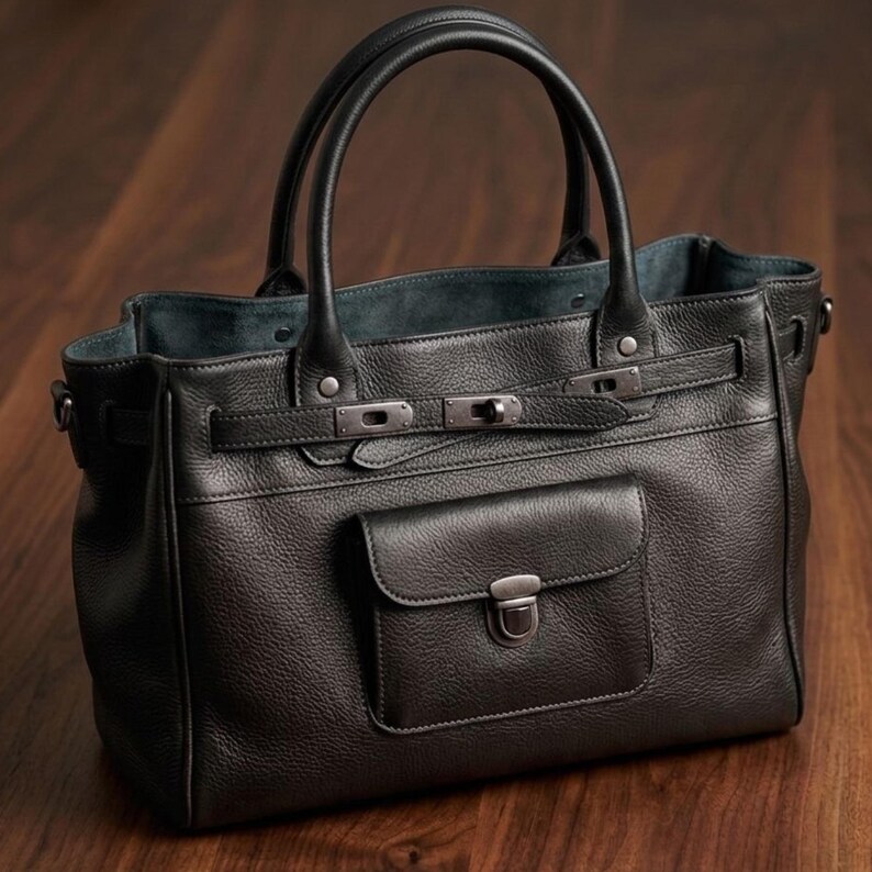 May include: A black leather handbag with a textured finish. The bag features two top handles, a front pocket with a clasp, and silver-toned hardware. The bag has a rectangular shape and a structured design.