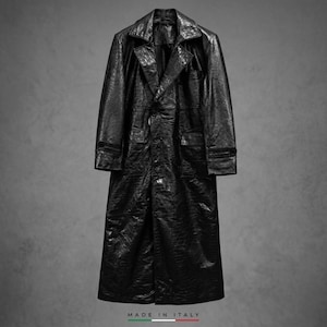 Può includere: Un cappotto lungo nero con una finitura testurizzata e lucida, caratterizzato da un ampio colletto, chiusura frontale con bottoni e due tasche anteriori. Il capo presenta un motivo sottile e ripetitivo. Il testo MADE IN ITALY è stampato sotto.