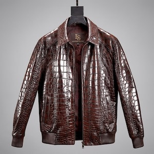 May include: A dark brown jacket with a glossy, embossed crocodile skin texture. The jacket features a classic collar, a front zipper closure, ribbed cuffs and hem, and a dark interior lining with the text LS LEATHER STUDIO on the label.