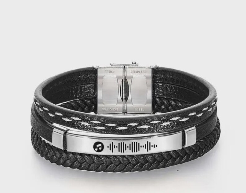 May include: Black leather bracelet with a stainless steel clasp and a silver plate featuring a music note and a sound wave design. The bracelet has multiple layers with braided and stitched details.