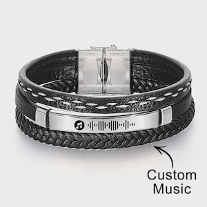 May include: Black leather bracelet with a stainless steel clasp and a silver plate featuring a music-themed design. The bracelet has multiple layers and a braided band. The text "Custom Music" is also visible.