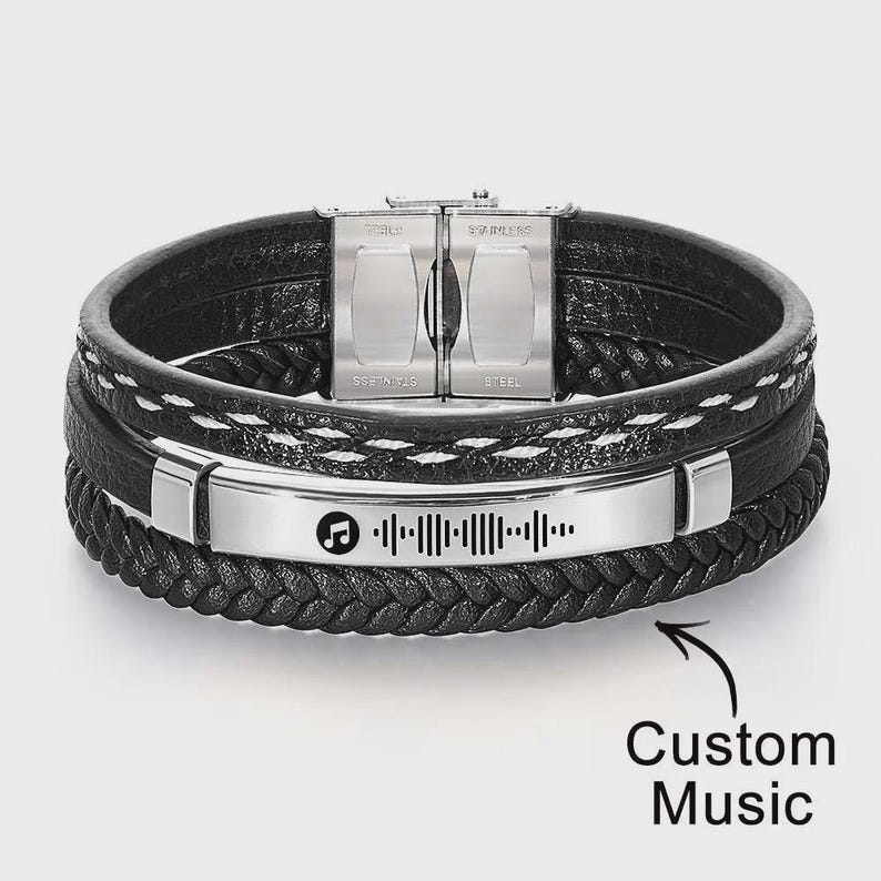 May include: Black leather bracelet with a stainless steel clasp and a silver plate featuring a music-themed design. The bracelet has multiple layers and a braided band. The text "Custom Music" is also visible.