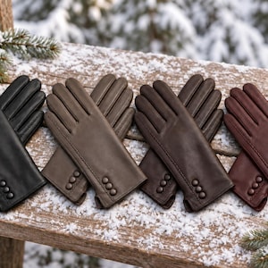 May include: Four pairs of leather gloves in black, light brown, dark brown, and reddish-brown. Each pair features three small matching buttons on the wrist area, visible stitching along the fingers, and a smooth finish on the exterior surface.