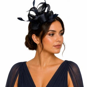 May include: A navy blue headpiece with a layered design and delicate feathers. The headpiece is worn by a person wearing a navy blue dress with a V-neckline and cape sleeves. The background is white.