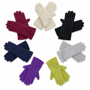 Könnte beinhalten: Eine Sammlung von sieben Paar Strickhandschuhen, die kreisförmig angeordnet sind, in den Farben Bordeaux, Creme, Schwarz, Marineblau, Violett, Limettengrün und Grau. Jedes Paar Handschuhe ist mit drei kleinen Zierknöpfen am Handgelenk versehen.