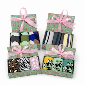 May include: Four rectangular gift boxes with floral patterns, each tied with a pink ribbon. The boxes contain various pairs of socks featuring patterns including leopard print, zebra stripes, panda illustrations, and geometric colour blocks.
