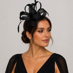 Peut inclure: Coiffe noire avec un motif de nœud et des accents de plumes. Le couvre-chef est porté sur la tête et est fait d'un matériau en tissu. La femme de l'image porte une robe noire avec un décolleté en V.