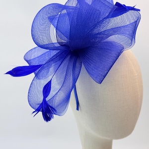 May include: A vibrant blue headpiece featuring a large, layered mesh bow and delicate feathers. The headpiece is mounted on a neutral-toned mannequin head, showcasing its shape and design. This accessory is suitable for special occasions.