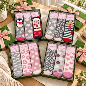 May include: Four gift boxes containing sets of three pairs of fuzzy socks. The socks feature various patterns including penguins, Santa Claus, reindeer, snowflakes, leopard spots, polka dots, and hearts in colors like red, pink, gray, and white.