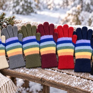 Peut inclure: Une rangée de sept gants en tricot, chacun présentant un motif de rayures arc-en-ciel horizontales sur les doigts et la paume. Les gants ont des poignets et des bouts de doigts unis en crème, gris, vert olive, bordeaux, rouge, bleu marine et noir.