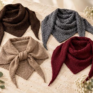 May include: Four triangular scarves in dark brown, charcoal grey, beige, and deep burgundy. Each scarf features a textured, knit construction with pointed ends. The beige scarf is tied in a knot at the centre, while the others are draped flat.