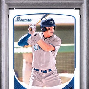 Puede incluir: Una tarjeta de béisbol con Aaron Judge de los Yankees de Nueva York con uniforme gris, sosteniendo un bate. La tarjeta está calificada y encapsulada, con texto que indica que es de 2013 Bowman DP & Pros.