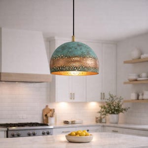 Könnte beinhalten: Eine hängende Pendelleuchte in Türkis und Kupfer hängt in einer Küche. Die kuppelförmige Leuchte hat ein perforiertes Kupferband und eine messingfarbene Oberseite. Sie wird von einem schwarzen Kabel abgehängt und beleuchtet die Küche.