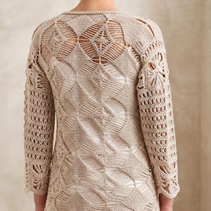 May include: A beige long-sleeved top featuring an intricate crochet pattern composed of repeating diamond-shaped motifs. The garment has a round neckline and three-quarter length sleeves, showcasing a detailed openwork design throughout the fabric.