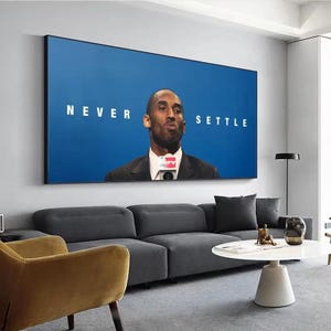 May include: A rectangular wall art print featuring a portrait of a man in a dark suit and white shirt against a solid blue background. The text NEVER SETTLE is printed in white capital letters on either side of the man's head.