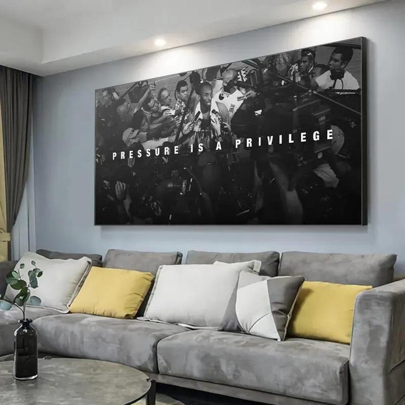 Op de afbeelding: Een rechthoekige zwart-wit wandkunstprint met een menigte mensen met camera's en microfoons rondom een centrale figuur, met de witte tekst PRESSURE IS A PRIVILEGE gecentreerd in het midden van de compositie.
