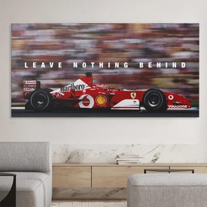 May include: A rectangular wall art print featuring a red Formula One race car in motion on a track. The car displays white sponsor logos and the text LEAVE NOTHING BEHIND in white capital letters centered above the vehicle against a blurred background.