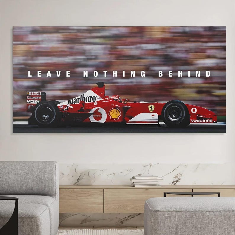 May include: A rectangular wall art print featuring a red Formula One race car in motion on a track. The car displays white sponsor logos and the text LEAVE NOTHING BEHIND in white capital letters centered above the vehicle against a blurred background.