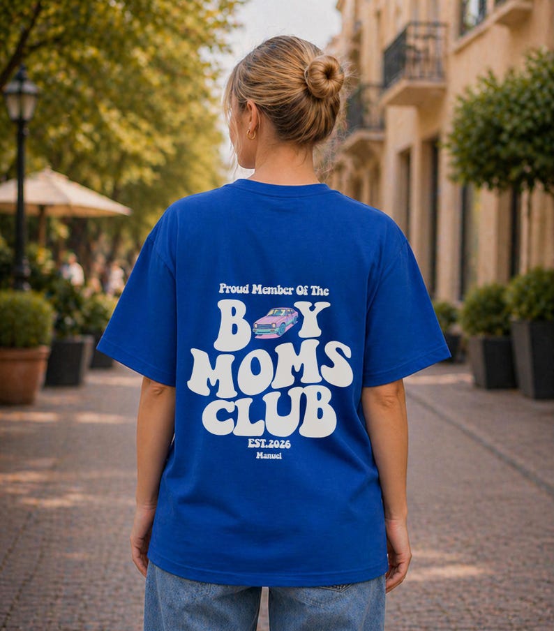 May include: A royal blue t-shirt with white text that reads "Proud Member Of The Boy Moms Club." The graphic includes a pink and blue car illustration. The shirt also has the text "EST.2026 Manuel."