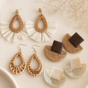 May include: A collection of handmade earrings in various styles. The earrings feature woven rattan and raffia materials in natural tones, with some designs incorporating white fringe and wooden accents. The earrings are displayed on a neutral surface.