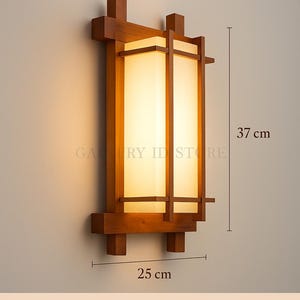 Puede incluir: Lámpara de pared decorativa de estilo japonés. La lámpara rectangular está hecha de madera de teca marrón nogal y presenta una pantalla de acrílico. La lámpara mide 25 cm de ancho y 37 cm de alto.