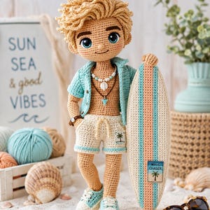 Könnte beinhalten: Gehäkelte Puppe eines Surferjungen mit blonden Haaren, blauen Augen und einem türkisfarbenen Hemd. Er hält ein Surfbrett mit blauen, pfirsichfarbenen und weißen Streifen. Die Puppe trägt Shorts und Turnschuhe. Der Hintergrund umfasst Muscheln und ein Schild mit der Aufschrift "Sun Sea & good Vibes".