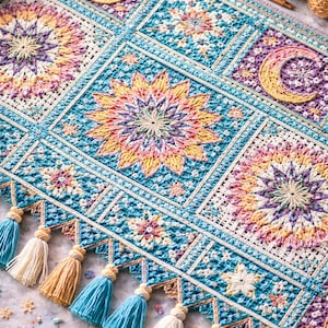 Może przedstawiać: Kolorowy, ręcznie robiony koc z szydełka z niebiańskimi wzorami. Koc ma turkusowe tło z kwadratami słońc, księżyców i kwiatowych wzorów w odcieniach różu, żółci i fioletu. Jest wykończony frędzlami.