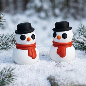 May include: Two small snowman figurines with black top hats, orange noses, and red scarves. The snowmen have black button eyes and are set in a snowy environment with evergreen branches in the background. The snowmen are a festive holiday decoration.