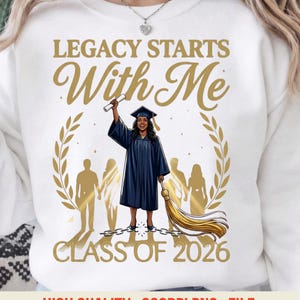 May include: White sweatshirt with a graphic of a graduate in a blue gown holding a diploma and tassel. The text reads "LEGACY STARTS With Me CLASS OF 2026". Gold laurel wreath and silhouette figures are also present.
