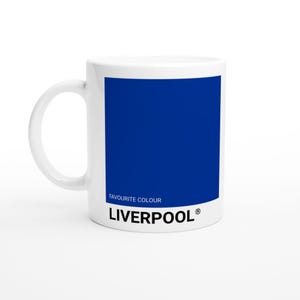 May include: White ceramic mug with a blue square and the text "FAVOURITE COLOUR" and "LIVERPOOL®" printed on it. The mug has a curved handle and a glossy finish. The mug is a fan item.