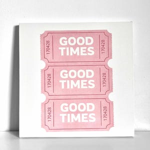Könnte beinhalten: Ein weißer Leinwanddruck mit drei rosa Ticketabschnitten. Jeder Abschnitt trägt die Worte "GOOD TIMES" in fetten weißen Buchstaben. Die Nummer "170428" ist vertikal auf jedem Abschnitt gedruckt.