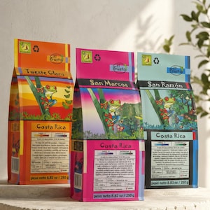 Peut inclure: Trois sachets de café rectangulaires étiquetés El Gusto Costa Rica, illustrés d'une rainette aux yeux rouges. Les sachets sont orange, rose et bleu clair, avec des textes comme San Marcos, San Ramon et Tueste Claro, pesant 250 g chacun.