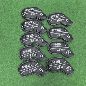 Op de afbeelding: Een verzameling zwarte golfclubhoezen met witte stiksels en letters. Elke hoes is gemarkeerd met "PING G730" en een nummer of letter, waaronder 5, 6, 7, 8, 9, P, U, 50 en 56. De hoezen liggen op een groene ondergrond.
