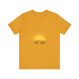 May include: Mustard yellow t-shirt featuring a yellow sun graphic with radiating lines and text in Hebrew. The short-sleeved shirt is made of a soft material.